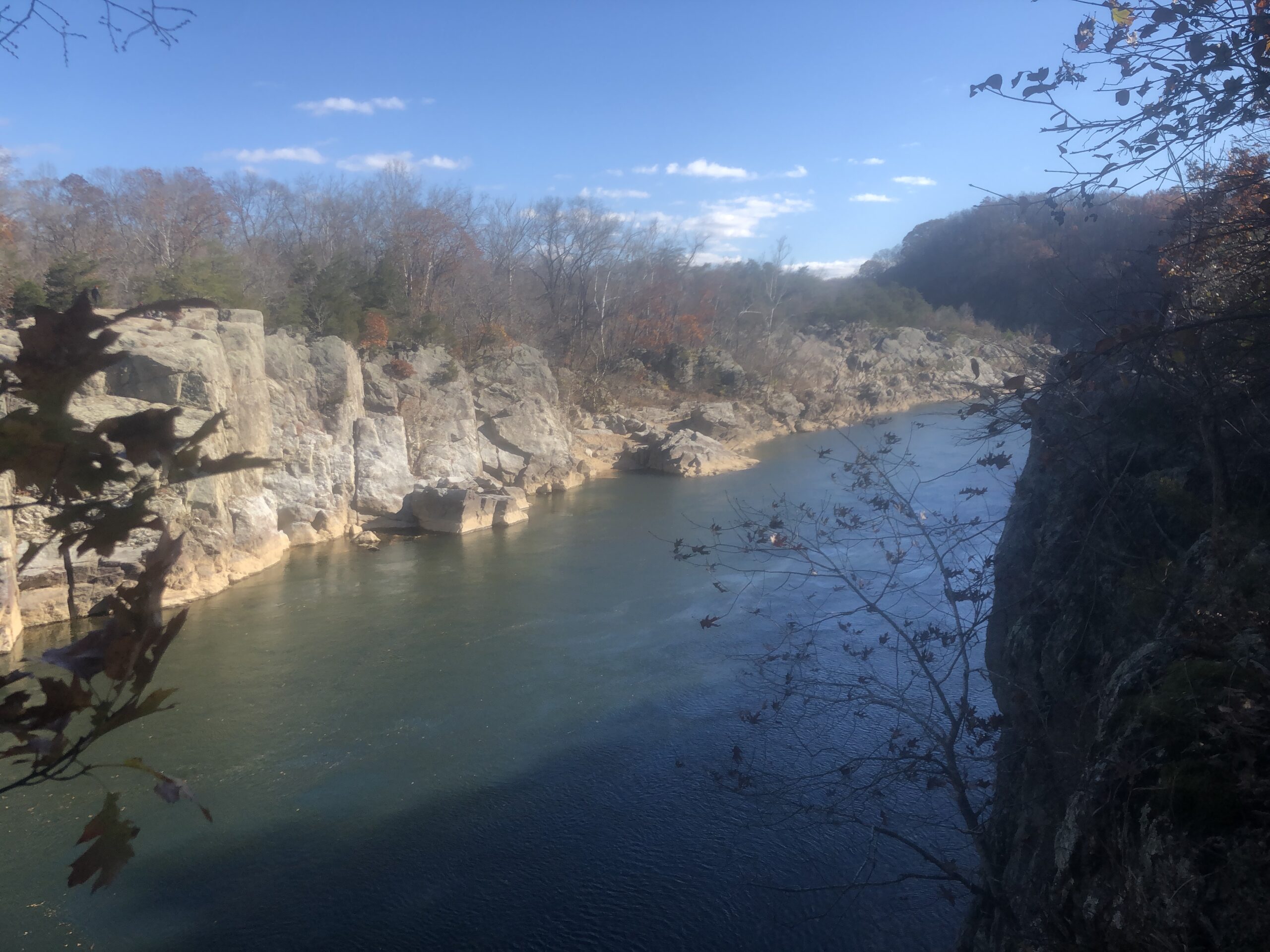 Potomac River flowing through boulders and cliff with trees and brush on top. 