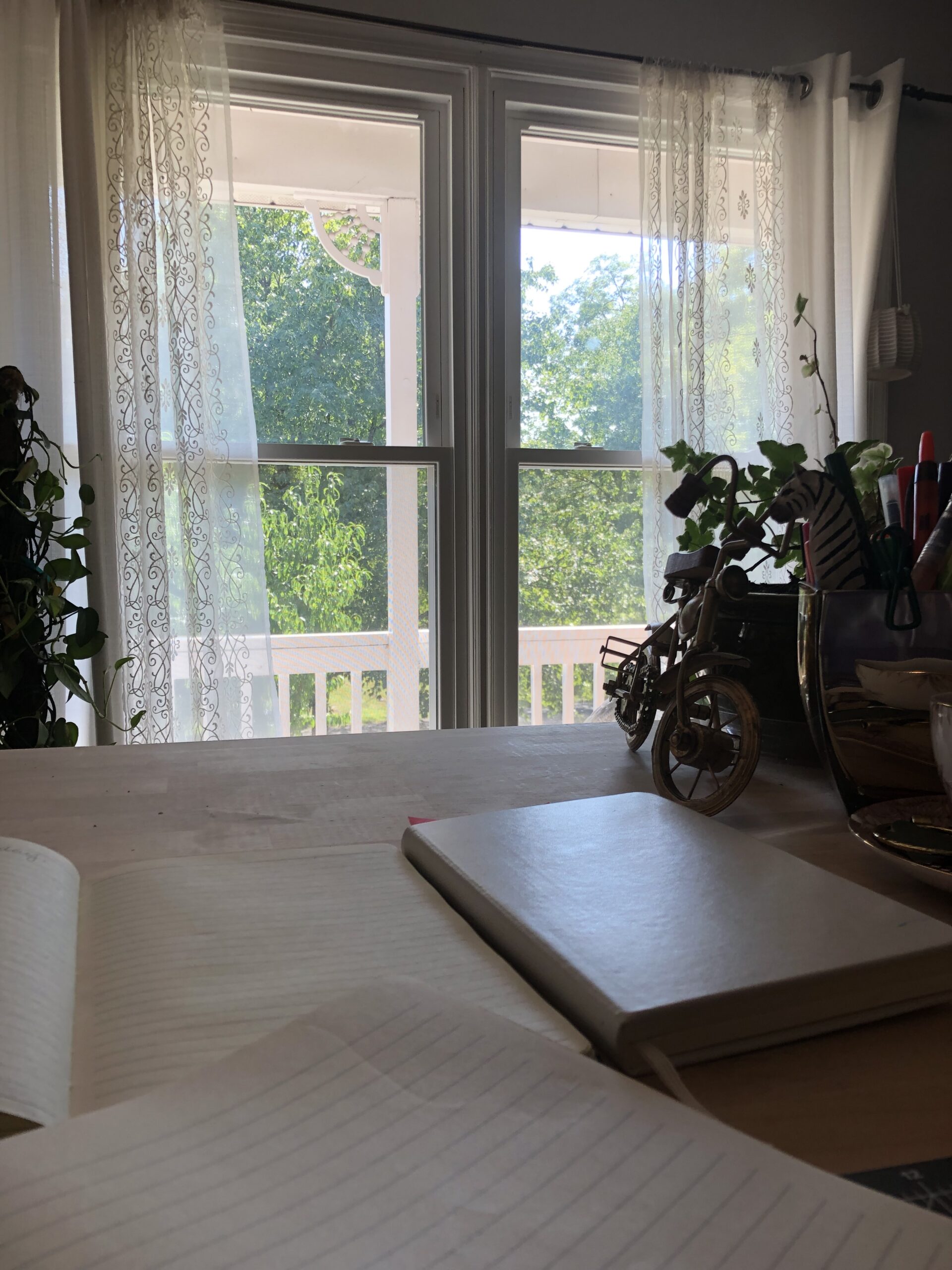desktop with blank paper and journal with a plant and open window in the background