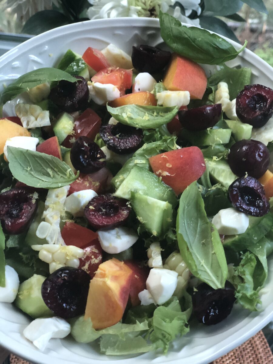 salad with peaches, cherries, cucumber, corn and basil in a white bowl
